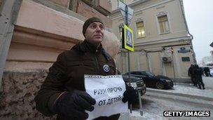 A man holds a poster reading: 'Hands off children!' as he protests against a bill banning Americans from adopting Russian children