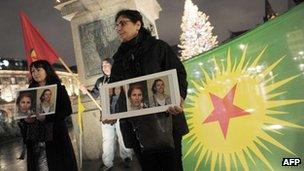 A woman of Kurdish origin holds a frame with photos of three Kurdish women activists