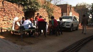 Farmers in a rural area in India sitting in front of a luxury car