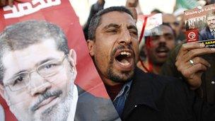 Man at a demonstration holds up a poster of Mohammed Morsy