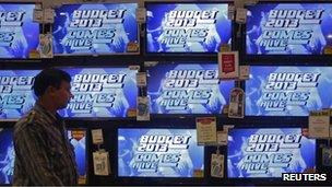 A man walks past television screens showing an advertisement for a program on India"s annual budget at an electronics shop in Mumbai in this February 22, 2013