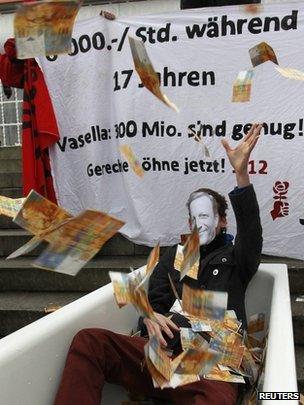 A protester wearing a mask with Vasella portrait throws fake banknotes during a demonstration before Swiss drug maker Novartis annual shareholders general meeting in Basel