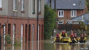 Firefighters pull a boat as they wade down a flooded street in St Asaph