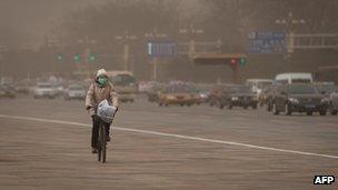 A woman cycles past traffic during a sand storm in heavily polluted weather in Beijing, 28 February 2013