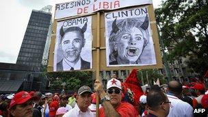Man holds a protest sign with Hillary Clinton and Barack Obama made to look like demons