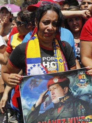 A woman weeps as she holds a picture of President Chavez