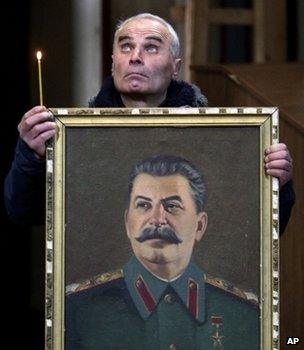 Georgian man holds a candle and a portrait of Joseph Stalin in a church in Gori