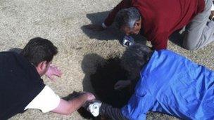 Hank Martinez, top, Ed Magaletta, right, and Russ Nobbe, look into an 18-foot-deep and 10-foot- wide sinkhole for golfer Mark Minhal 8 March 2013