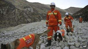 Rescuers lead sniffer dogs while searching through rock and debris at a gold mine after a mudslide in Gyama village, in Maizhokunggar County of Lhasa, Tibet, 30 March 2013
