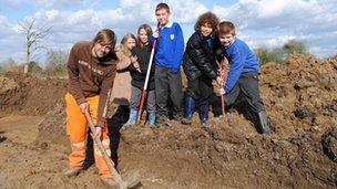 Children and a workman digging on a patch of mud