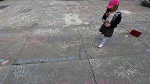 A girl walks amid chalk messages written by passerbys about the Boston Marathon bombing