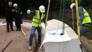 The stones are craned into position in the garden watched by the Bishop of Bath and Wells