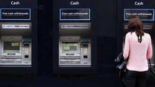 A woman uses one of a line of cash dispensers in central London