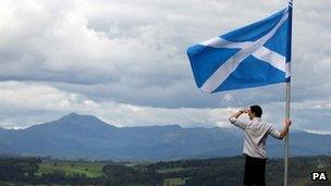 man holds saltire overlooking Scottish hills