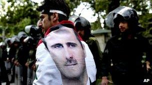 A man wrapped in a Syrian flag with a portrait of President Bashar Assad walks past riot police at an anti-Israeli rally in Tehran, Iran. Photo: 6 May 2013