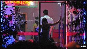 A woman awaits customers from the doorway of a neon-lit barber shop in Beijing on 9 July 2008