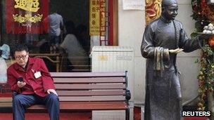 A man sits on a bench in front of a restaurant at a shopping district in Beijing