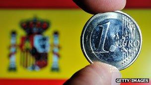 A euro coin being held up in front of a Spanish flag