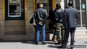 A group of people queue at an ATM outside the National Bank of Cyprus