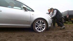 Two people pushing a car in a muddy field