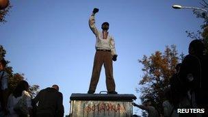 A protester gestures atop a garbage bin with the word 'Resign!' on it