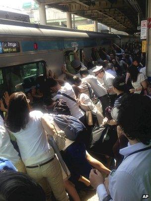 Train passengers and railway staff push a train car to rescue a woman stuck between the car and the platform at Japan Railway Minami Urawa Station in Saitama, near Tokyo, on 22 July 2013