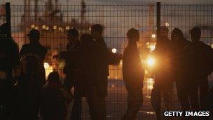 A group of people in shadow at a fence in Calais