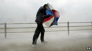 Walker battling wind and sea waves on a promenade seafront