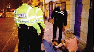 A woman sitting on the pavement as three police officers stand by