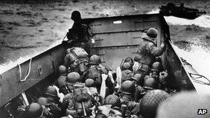 A landing barge, tightly packed with helmeted soldiers, approaches the shore at Normandy, France, on D-Day.