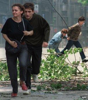 Sarajevo residents run through an intersection known for sniper activity after a shell fell in the center of the city on June 20, 1992.