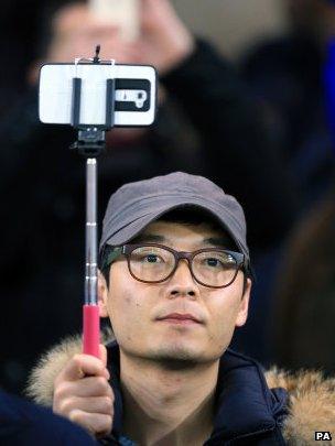 A football fan uses his selfie stick to hold aloft his smartphone