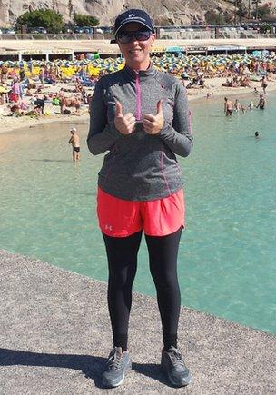 Laura at a beach wearing leggings, a long sleeved top and a cap