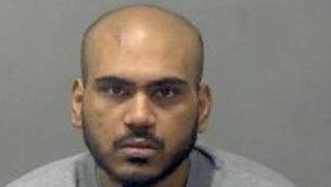 Abdul Kasim: a balding dark-haired man with a dark beard. He is wearing a grey, round-necked top, and looking straight ahead.