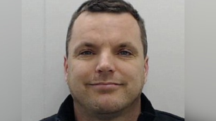 Man smiles at camera in mugshot.