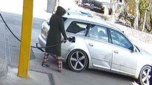 Person wearing long coat and pyjamas filling car with fuel