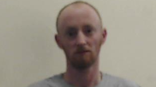 Blurry image of Christopher White in a grey T-shirt who is staring at the camera. He is balding and has a gingery beard.