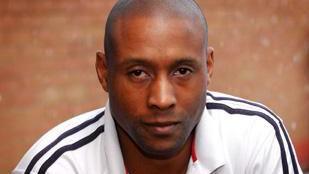 Jez Daniels, wearing a white top with black stripes on the shoulders and arms, looks at the camera