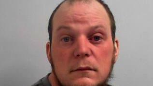 Custody image of Wiles, 36. He has a thinning chinstrap beard and high hairline. He looks like he might have been crying as his eyes and face are red.
