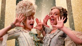 An Edwardian mother and daughter are posing and smiling in front of a glittery background
