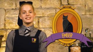 A girl in a school's uniform next to a framed picture of a black cat called Ember.