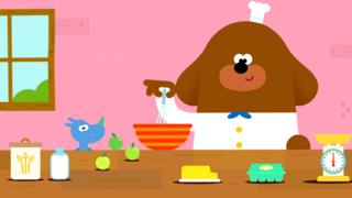 Hey Duggee wearing a chef uniform and cooking in a kitchen