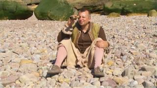 A pirate sat on a white stony beach, looking through a telescope