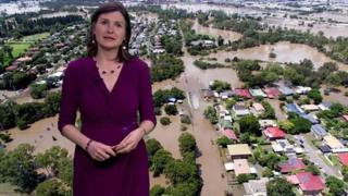 Helen Willetts stands in front of aeriel views of flooded suburbs in Australia