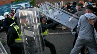 Protesters clash with police officers wearing riot gear during a demonstration in Southampton on Tuesday. Two officers in high vis use shields to push back people in the crowd wearing jackets and hoodies.