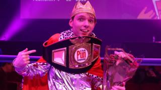 Adam Ernest Pickard bathed in purple light with a boxing-style belt around his shoulders