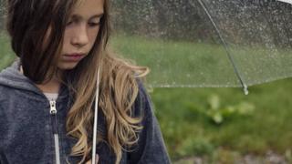 A girls standing under an umbrella in the rain