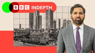 A montage image shows BBC economics editor Faisal Islam standing in front of a black-and-white image of Manchester's skyline. Islam is bearded with dark greying hair and wears a grey suit with a multicoloured tie and a white shirt. In the background is the BBC InDepth logo and a beige and a red backdrop.