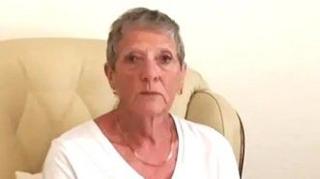 Woman sat on a sofa in a white top. She has grey hair.