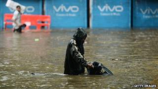 Indians wade through a flooded street during heavy rain in Mumbai